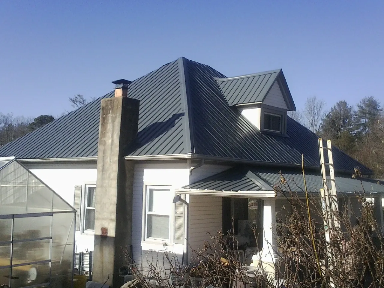 Dark blue standing seam metal roof on a white farmhouse with dormer — Slate & Tile Roof Repair by Roofing Brothers in Baldwinville