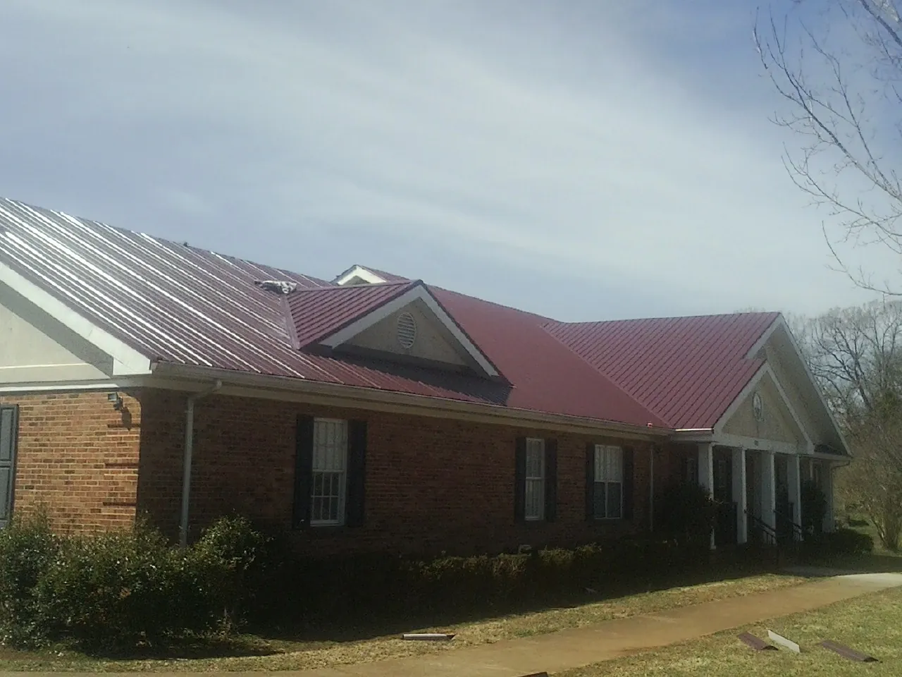 Red metal roof with gabled entries on a long brick building, from a Hail Damage Roof Repair job in Baldwinville