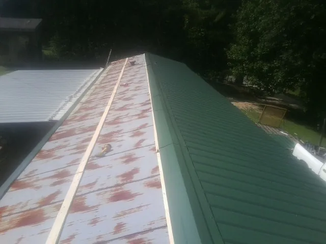 Old rusted panels beside newly installed green metal roofing — Wind Damage Roof Repair by Roofing Brothers in Baldwinville
