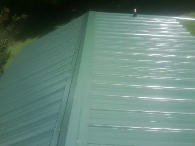 New green metal panels meeting at the ridge of a roof — Flat Roof Repair work by our crew in Baldwinville