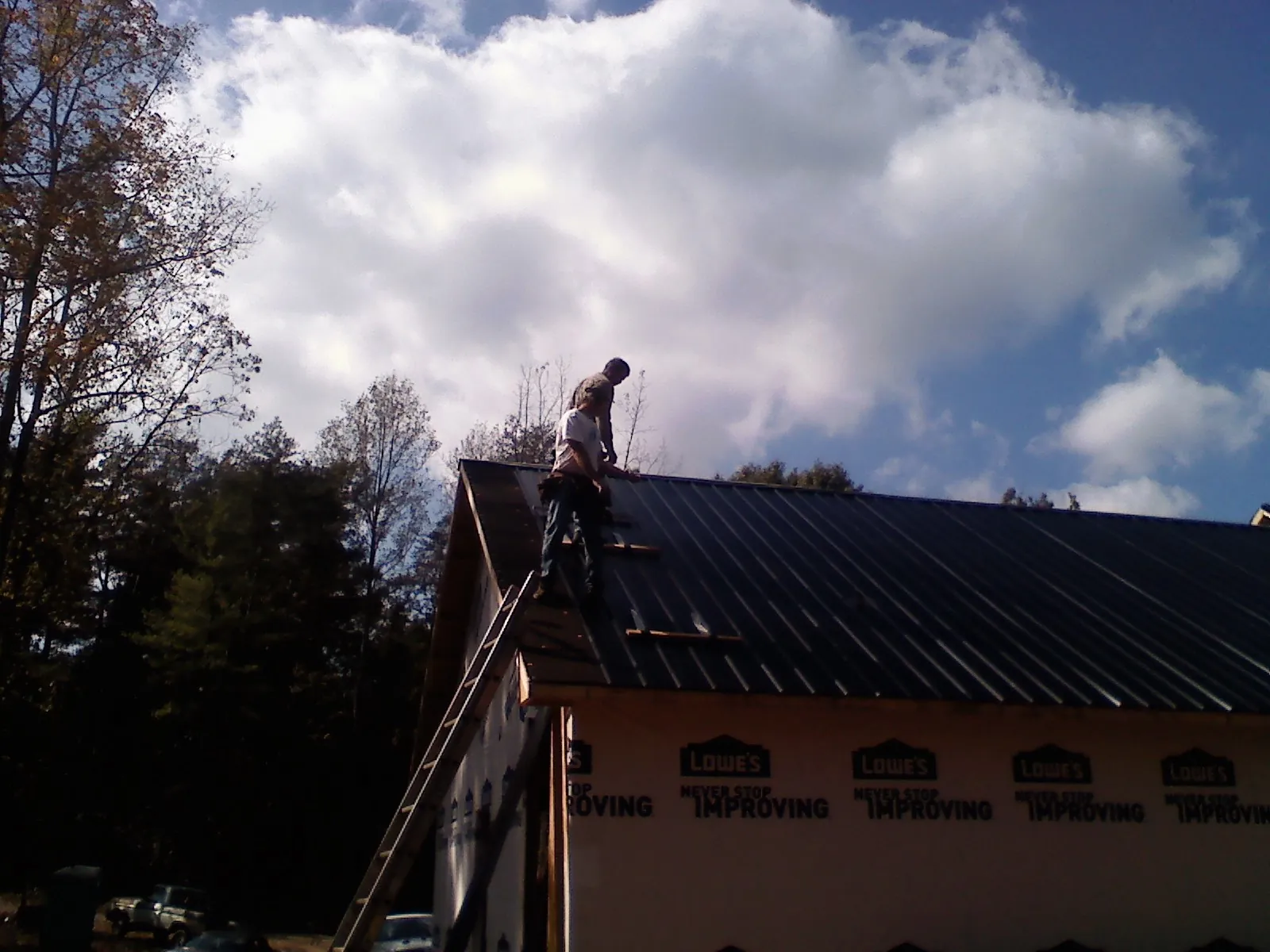 Roofer fastening dark metal panels high against a cloudy sky, from a Roof Inspection job in Baldwinville