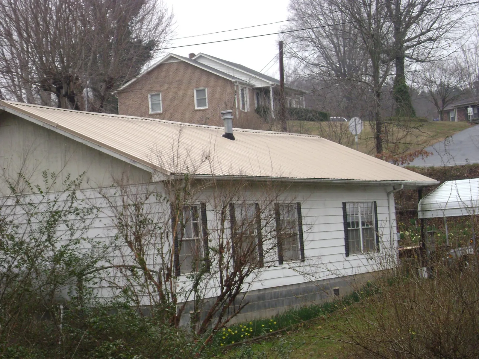 Tan metal roof on a white sided house set into a hillside — Commercial Roofing by Roofing Brothers in Baldwinville