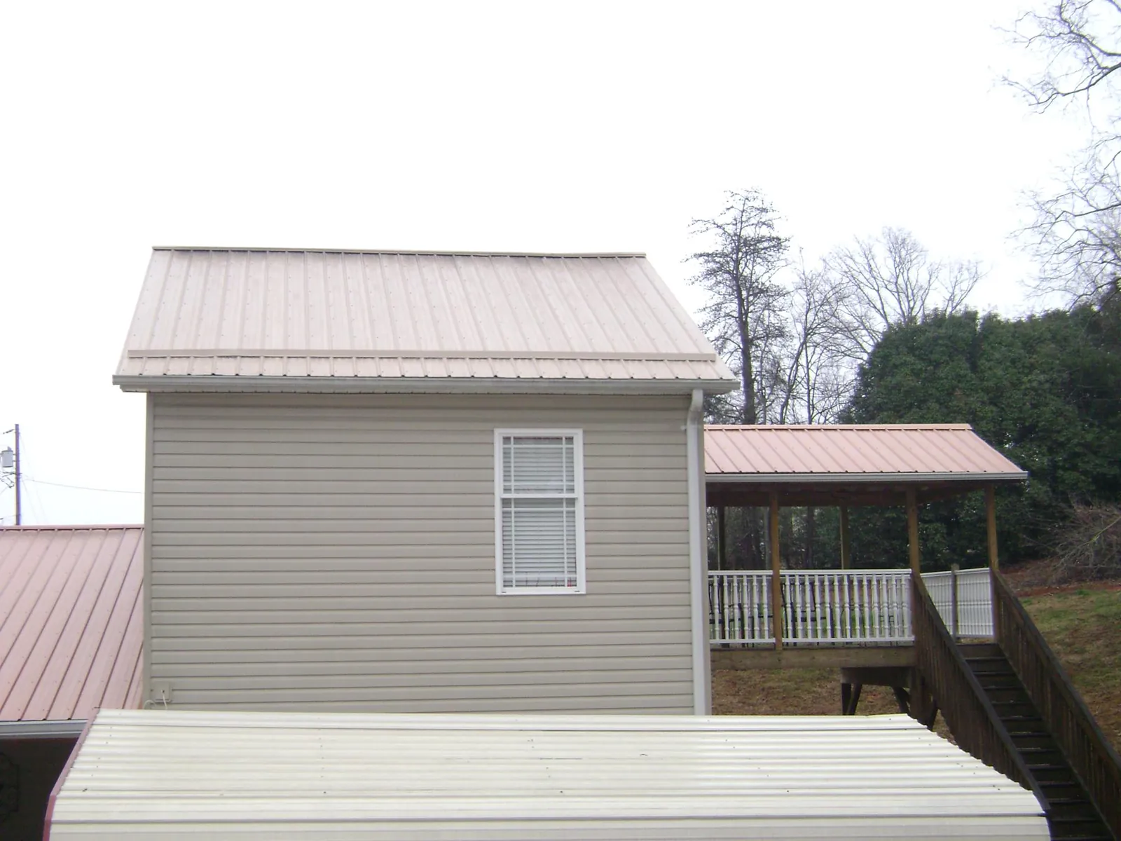 Tan metal roofs on a two story addition and attached porch, from a Roof Replacement job in Baldwinville