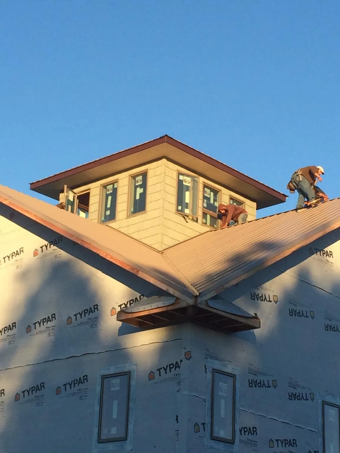 Roofers working around a rooftop cupola on a new metal roof at sunset — Roof Waterproofing in Baldwinville by Roofing Brothers
